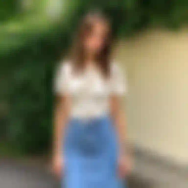 흰색 티셔츠와 데님 스커트를 입은 여성이 길에서 자신감 있게 포즈를 취하고 있다.