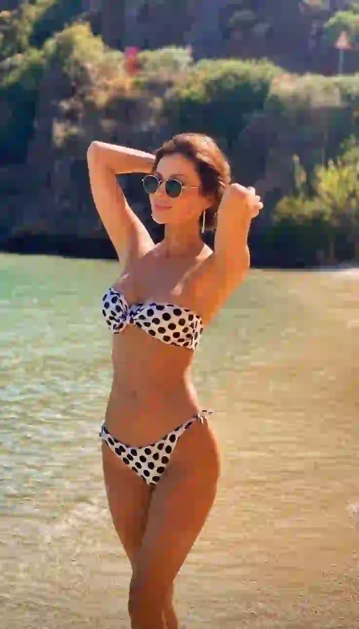 Una ragazza calda si pone in un bikini a pois sul mare, mostrando un cambiamento con i vestiti di AI rimodellamento.