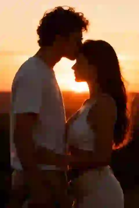 رجل ذو شعر مجعد يقبل جبهة المرأة عند غروب الشمس. تأثير لمولد صور التقبيل AI.