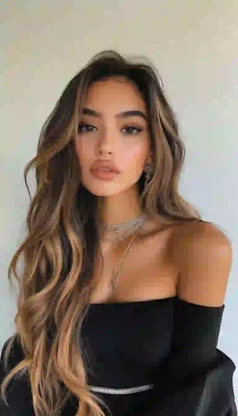 Mujer sexy con piel bronceada con vestido negro con hombros descubiertos posando en el interior.