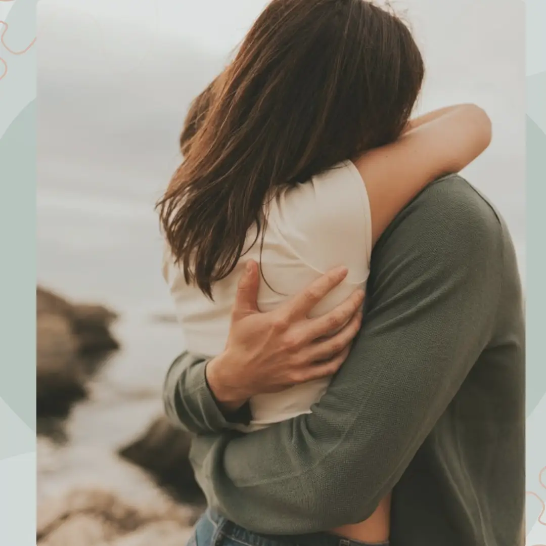 Um casal usa a ferramenta de vídeo Ai Hug, enquanto se abraçam em uma praia rochosa.