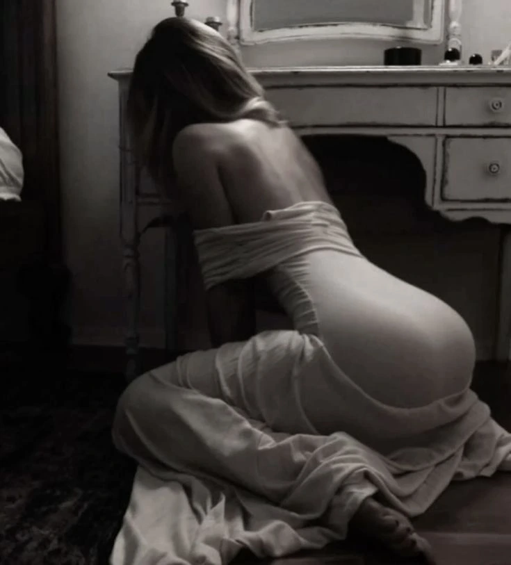 In una camera da letto scarsamente illuminata, una donna in una camicia da notte in pizzo si sporge in avanti, in ginocchio sul pavimento. In una camera da letto scarsamente illuminata, una donna in una camicia da notte in pizzo si sporge in avanti, in ginocchio sul pavimento.