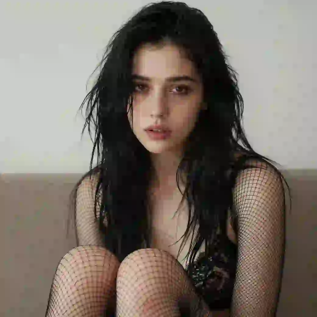 Donkerharige vrouw in zwart mesh-outfit poseert binnenshuis. Modelsjabloon voor photo face swap.