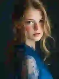 Portrait of a blonde woman with low ponytail and freckles staring at the camera. Template for Undress AI.