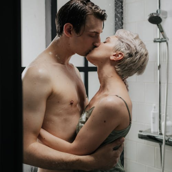 Photo of a kissing couple in the bathroom. The man is shirtless, and the woman's wearing a sleeveless green top.