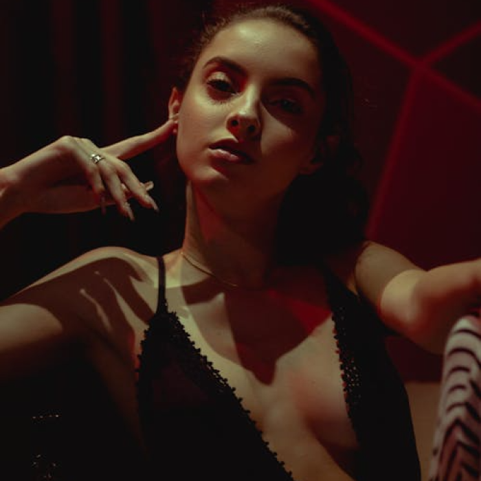 Portrait of a woman wearing a black tank top with a deep V-cut neckline that extends to her mid-torso, subtly revealing the outline of her chest.